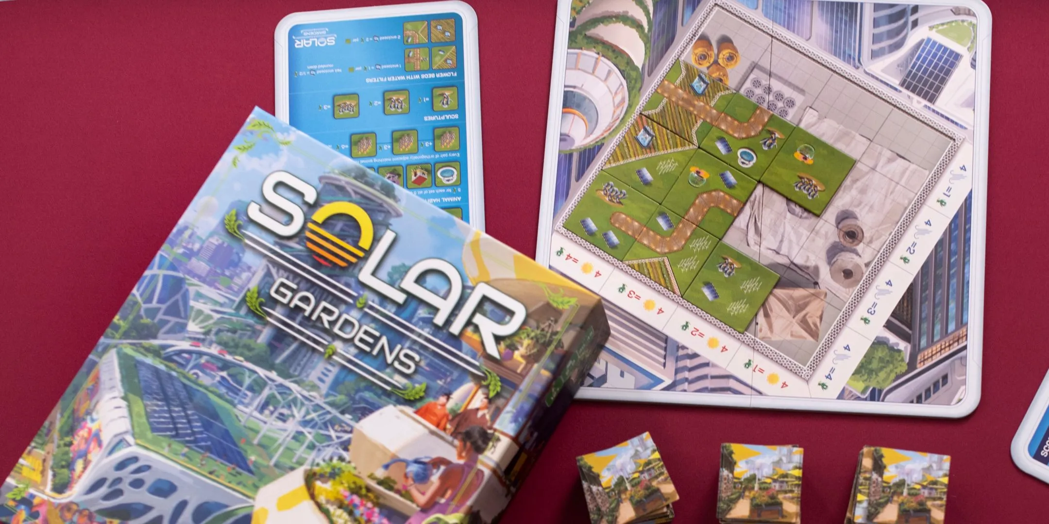 Hộp game và các thành phần của Solar Gardens được bày biện trên nền đỏ, tạo ấn tượng về sự chuyên nghiệp và thông điệp.