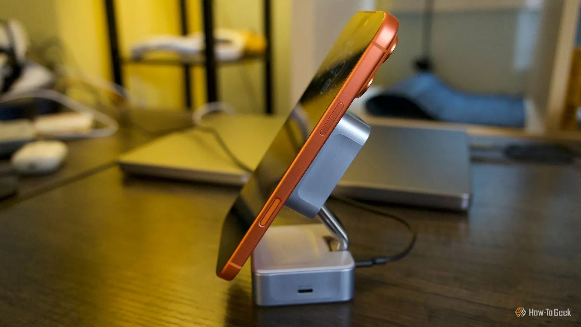 Ugreen MagFlow 2-in-1 ở chế độ dựng, kèm iPhone 17 Pro Max màu cam để minh họa vị trí sạc từ tính và không gian giữa các pad.